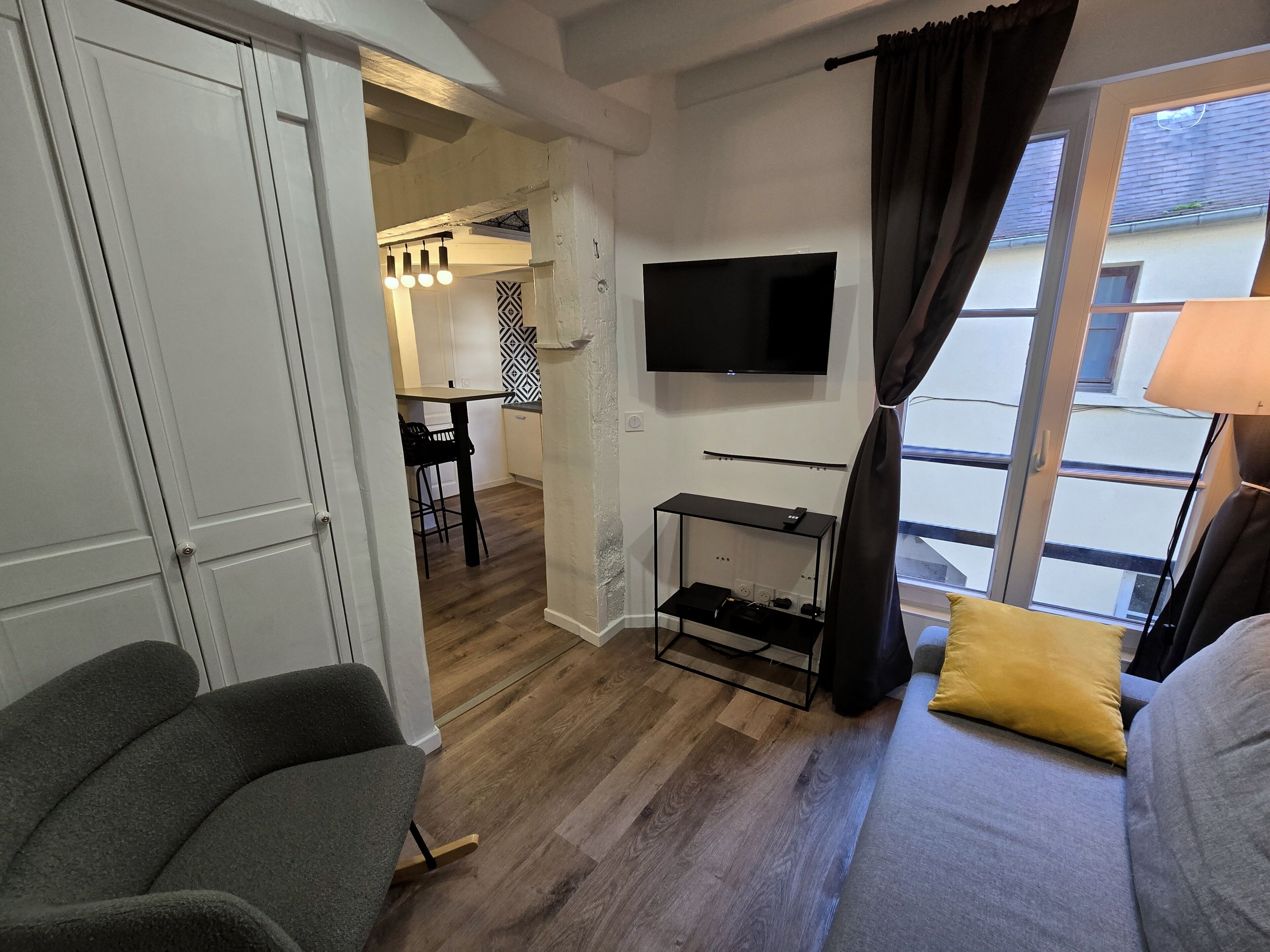 Una habitación con televisor, sofá, zona de comedor y balcón.