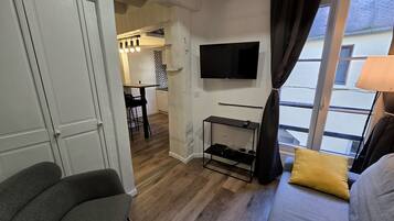 Una habitación con televisor, sofá, zona de comedor y balcón.