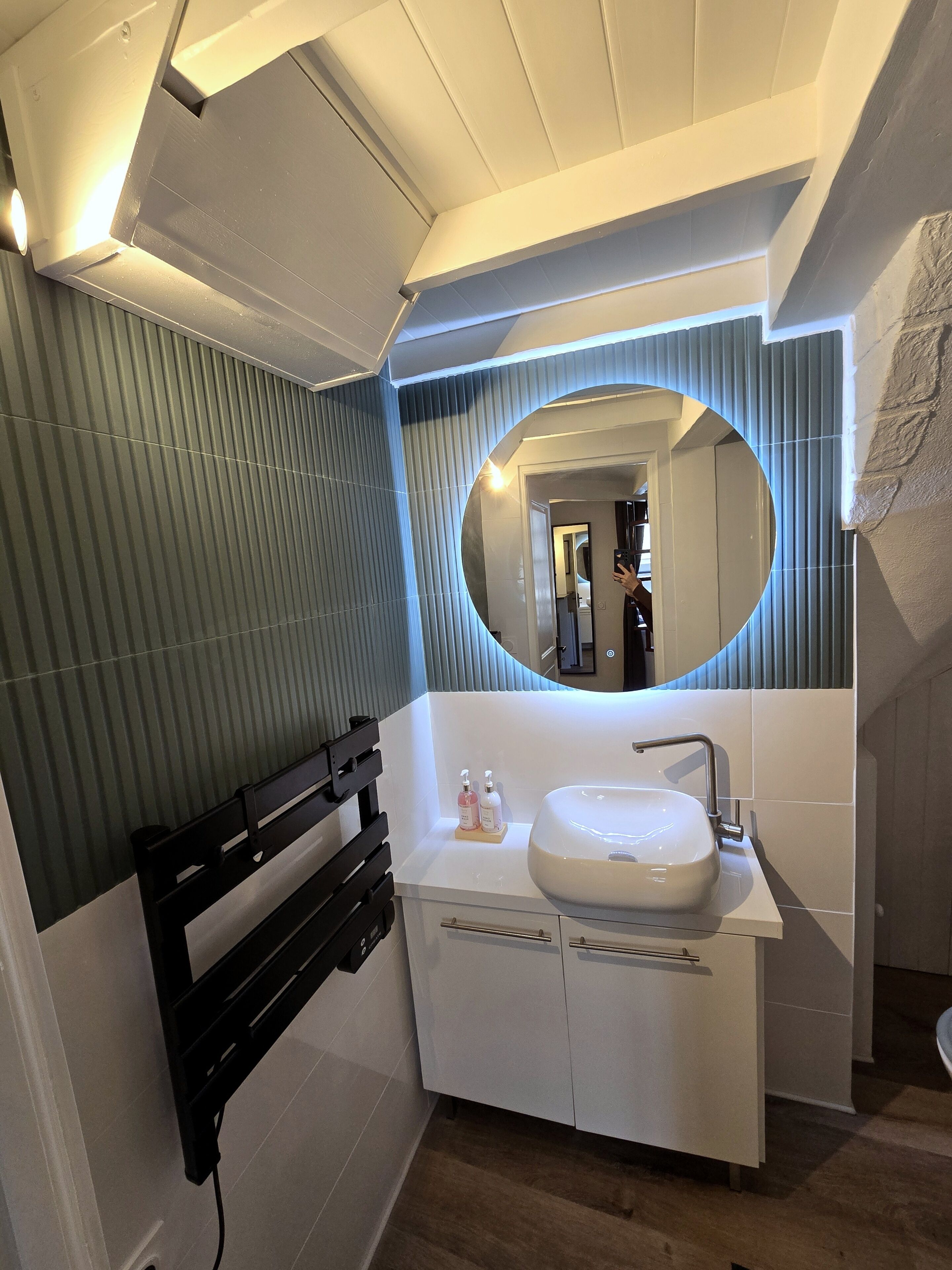 A modern bathroom with a white vanity, a round mirror, and a black towel rack.