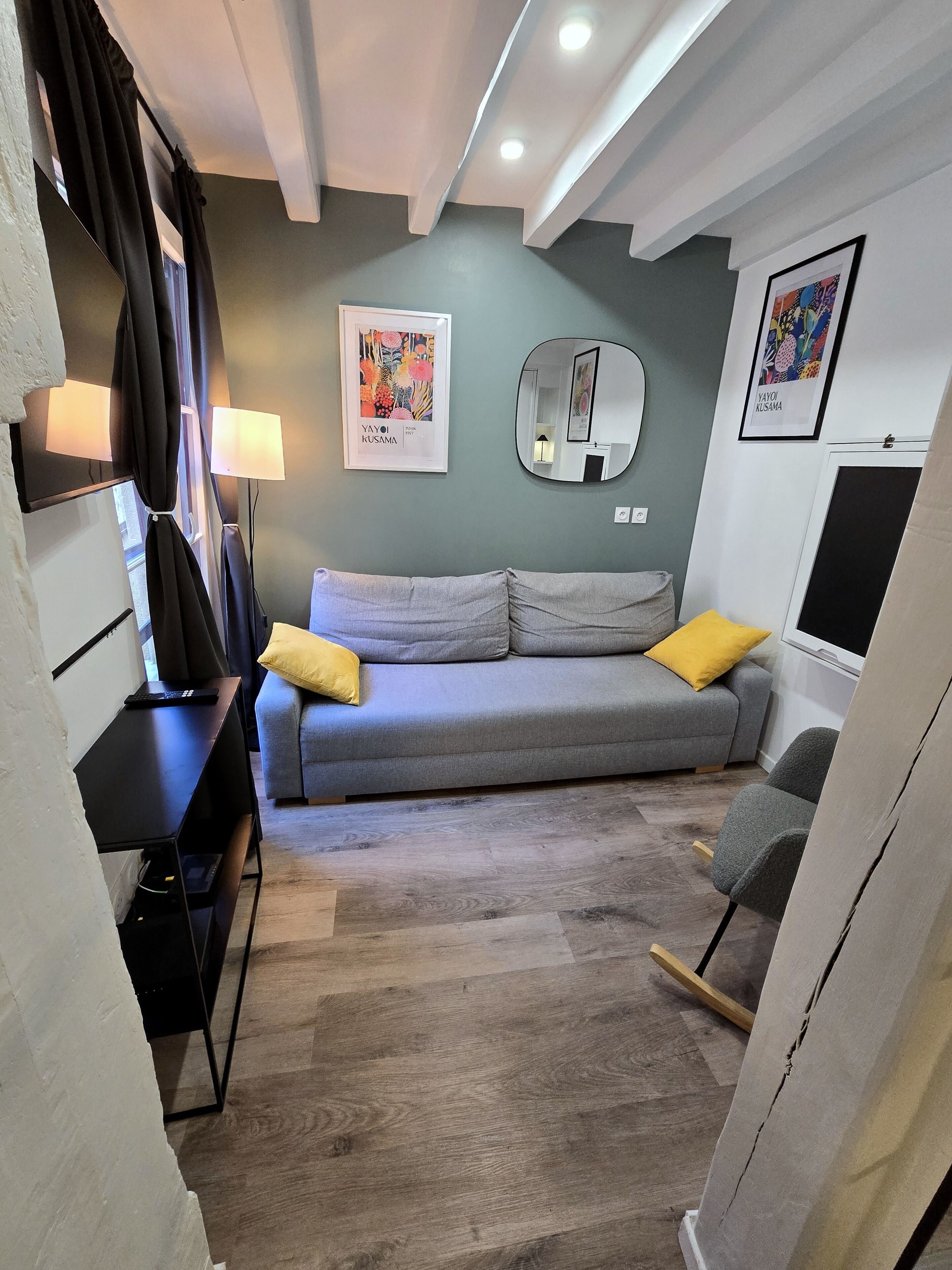 Een moderne woonkamer met een grijze bank, gele kussens, een zwart bureau, een spiegel en kunstwerken aan de wanden.