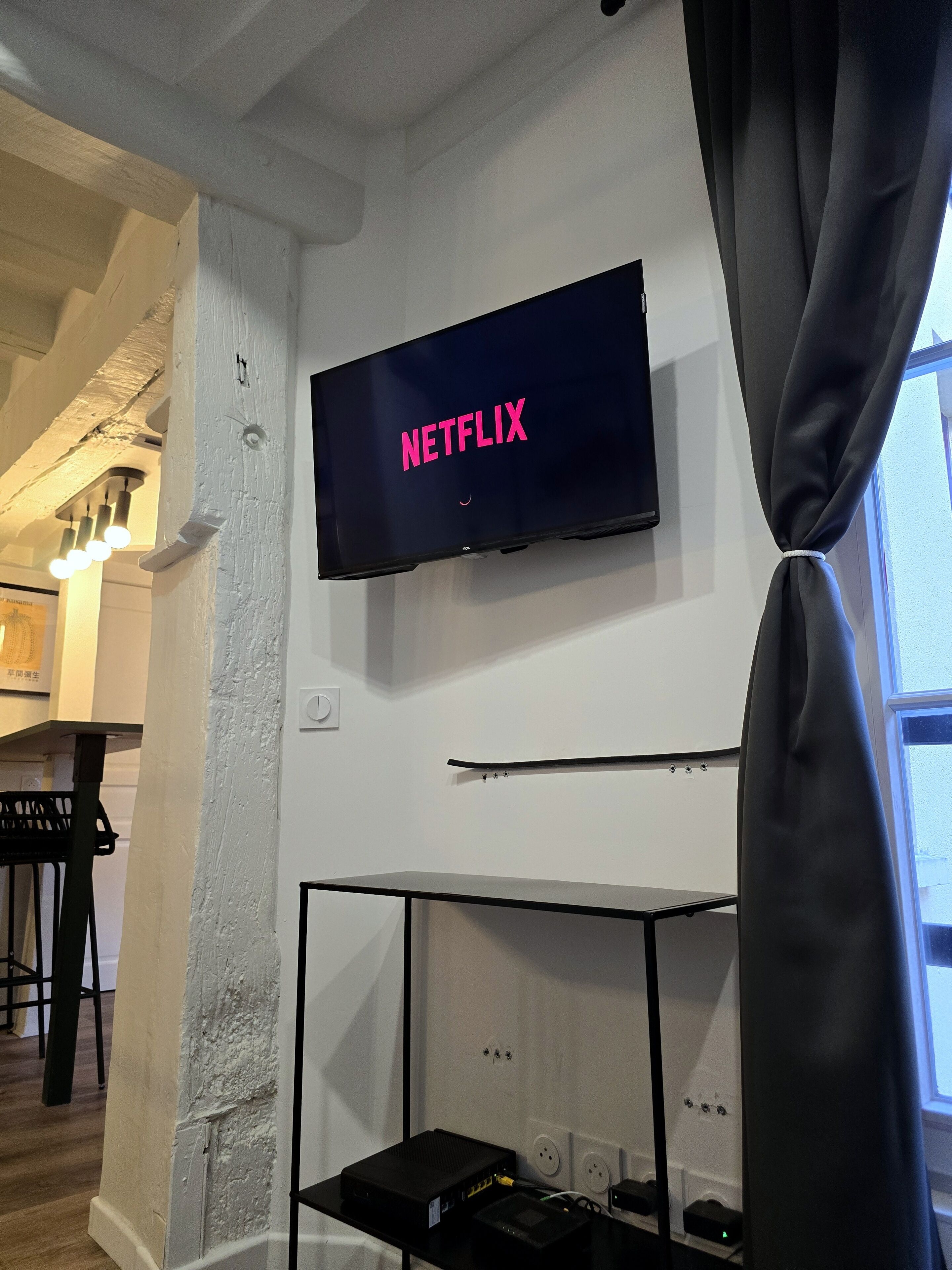 Habitación con televisión de pantalla montada mostrando 'NETFLIX', un piano y un mueble multimedia negro con dispositivos electrónicos.