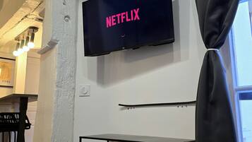 Habitación con televisión de pantalla montada mostrando 'NETFLIX', un piano y un mueble multimedia negro con dispositivos electrónicos.
