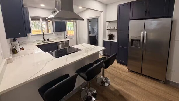 A modern kitchen with a central island, bar stools, dark cabinets, and a stainless steel refrigerator. - Modern Stay Next to Downtown  Sleeps 7 (San Antonio)