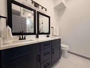 Ein Badezimmer mit einem Doppelwaschbecken, zwei Spiegeln, einer Toilette und einem weiß gefliesten Boden.