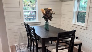 A dining area with a dark wooden table, four chairs, a vase with flowers, and a patterned rug. - Highly Rated Farm Cottage · Weatherford TX · 30 Min to Fort Worth (Weatherford)