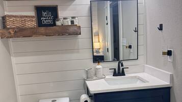 Een badkamer met een wit toilet, een donkerblauwe wastafel, een spiegel en een plank met planten en een bordje.