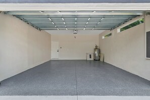 A garage with a concrete floor, a white door, and a metal roof structure. - Luxury New Home in Ybor's Heart (Tampa)