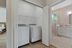 Een wasserij met twee wasmachines en een droogrek, grenzend aan een badkamer met een wastafel en aanrecht.