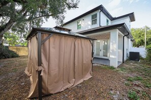 A modern two-story house with a covered outdoor area, a visible garage, and a well-maintained lawn. - Luxury New Home in Ybor's Heart (Tampa)