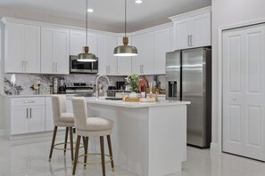 Cozinha moderna com armários brancos, eletrodomésticos de aço inoxidável e uma ilha central com banquetas.
