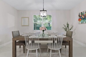 Ein Esszimmer mit Holztisch, weißen Stühlen, einer Blumenvase und einer Hängelampe.