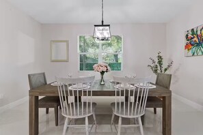Ein Esszimmer mit Holztisch, weißen Stühlen, Blumen in einer Vase und einem Gemälde an der Wand.