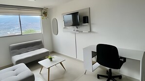 A modern room with a sofa, a small coffee table, a desk with a chair, a TV on the wall, and a window with a view. - 802 santa elena (Medellín)