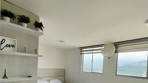 A modern bedroom with a bed, a sofa, a small table, a shelf with plants, and a sign that says 'Love'. - 802 santa elena (Medellín)