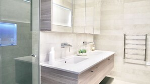 Un bagno moderno con cabina doccia in vetro, lavandino bianco, specchio e porta asciugamani.