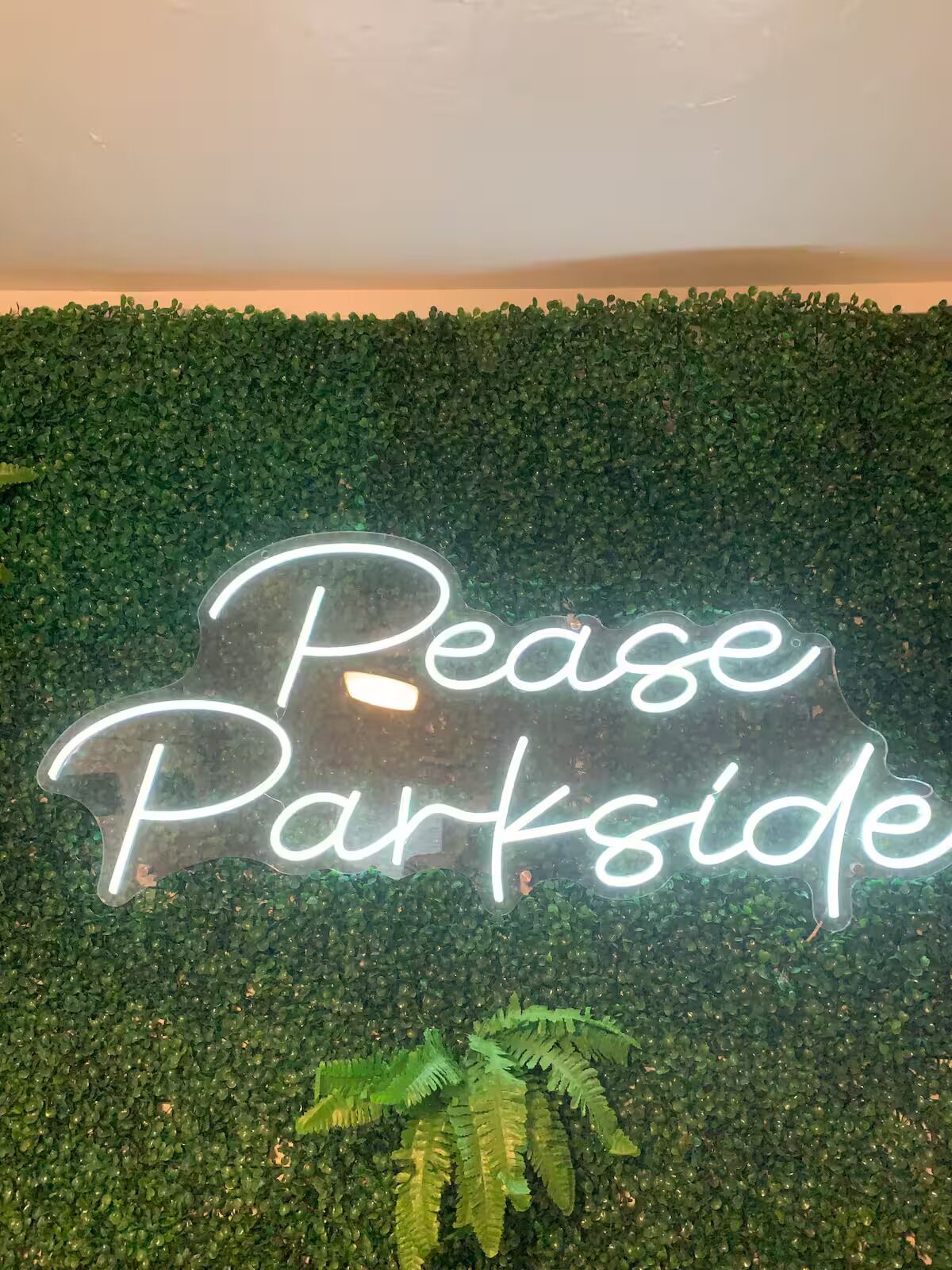 En neonskilte med teksten 'Rease Parkside' mod en baggrund af grønt løv.