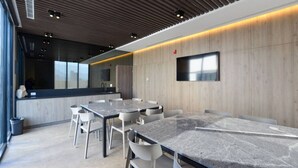 Ein moderner Konferenzraum mit einem langen Tisch, weißen Stühlen, einem Flachbildfernseher und einer Wand mit Holzvertäfelung.