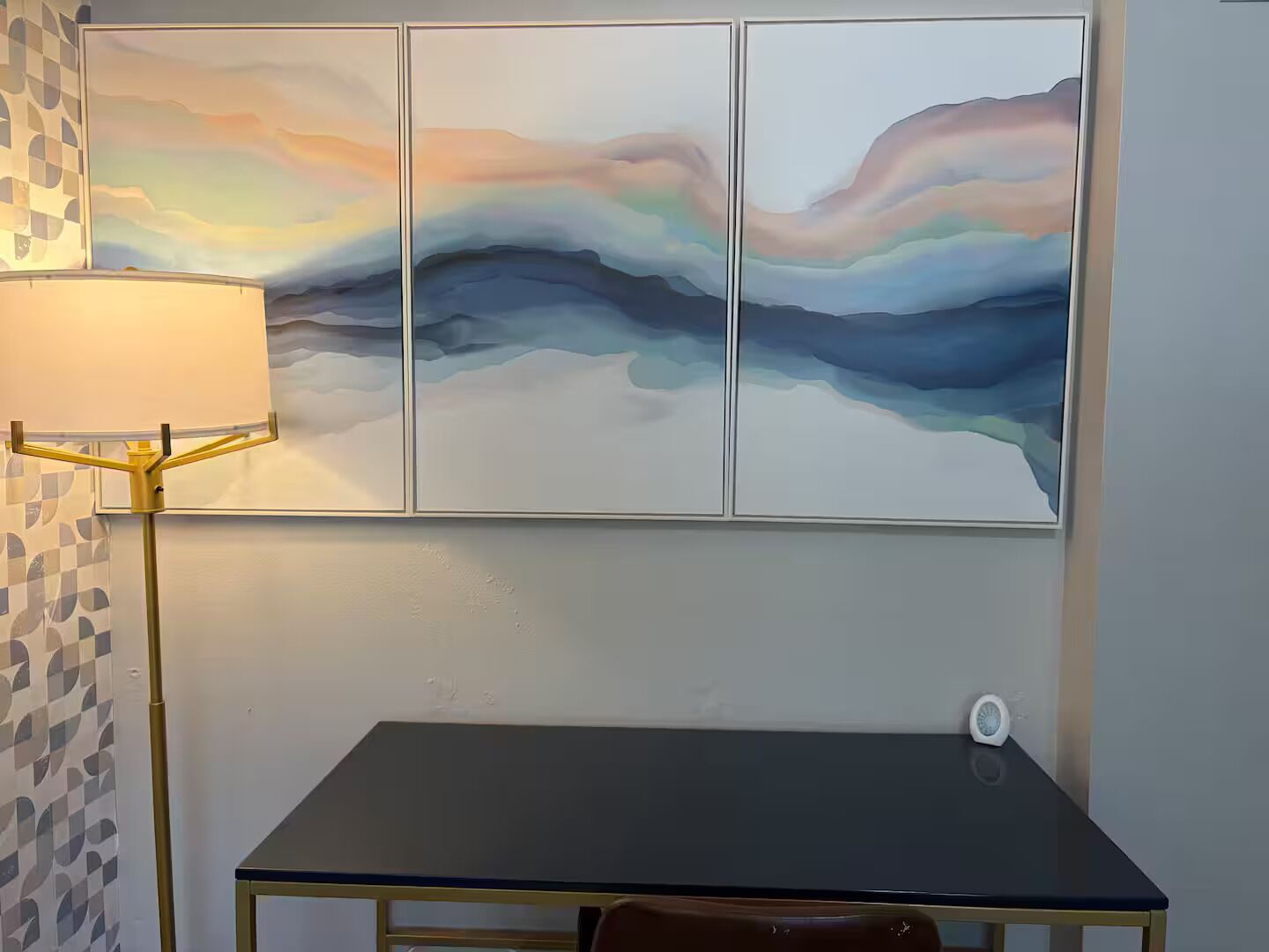 A room with a table, a lamp, and a wall-mounted abstract painting.