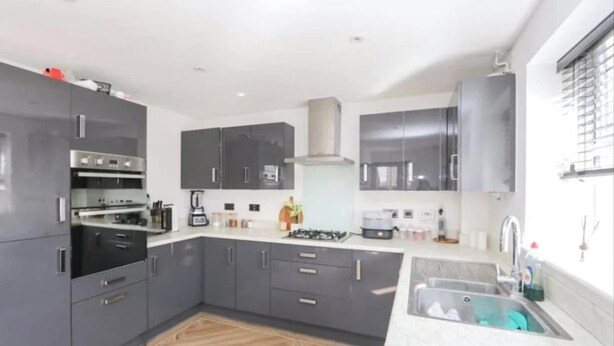 Una cucina moderna con mobili grigi, forno integrato, piano cottura a gas e lavello in acciaio inossidabile.