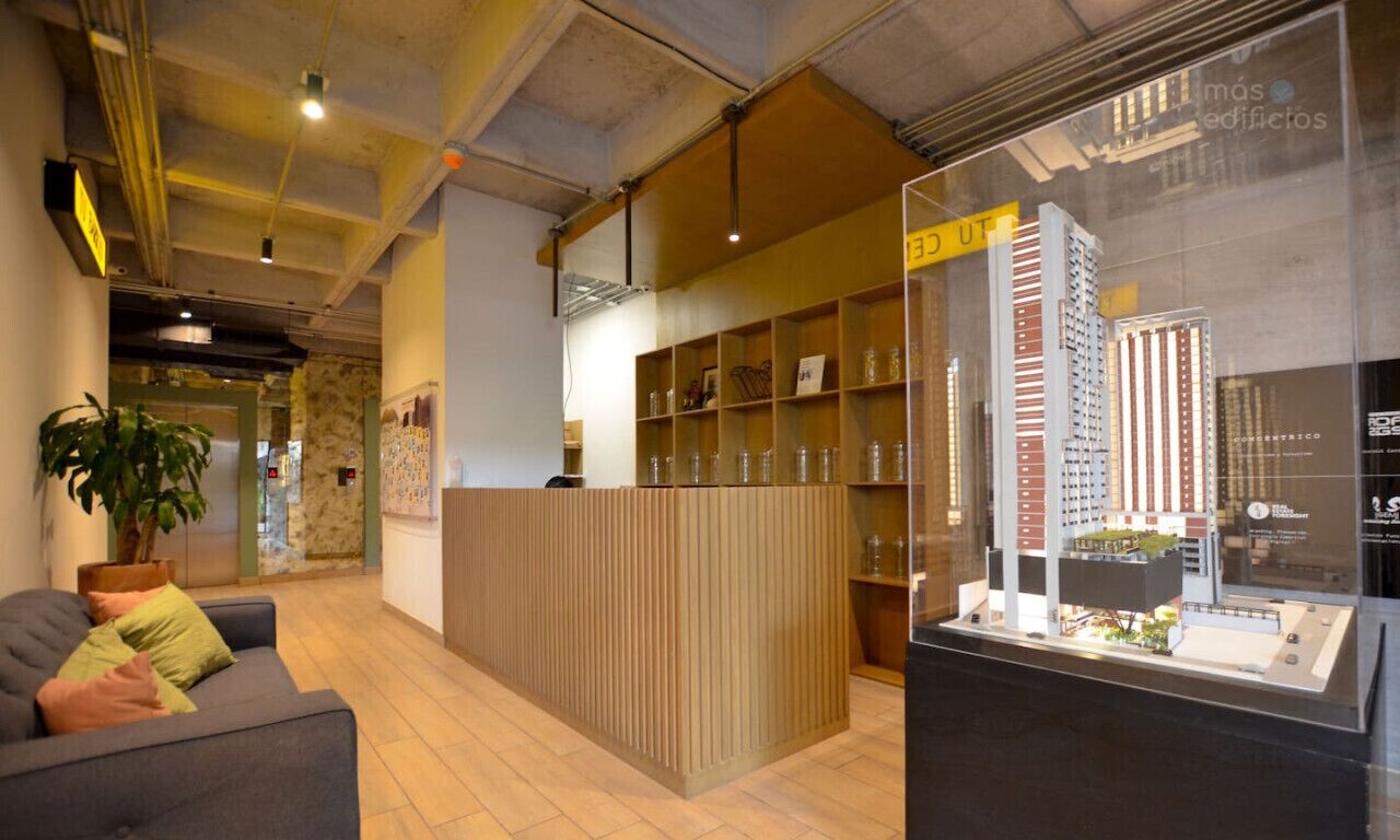 A reception area with a wooden reception desk, a glass display case with a model building, and a sofa with cushions.