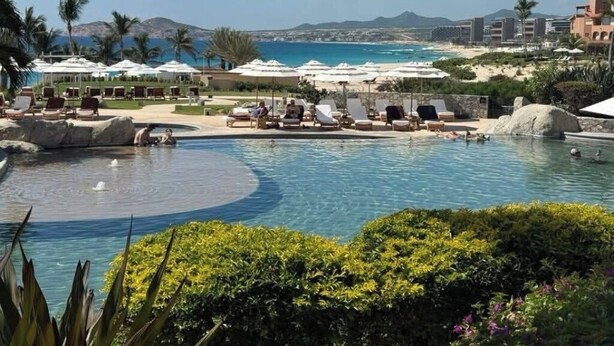Un complejo turístico con piscina, tumbonas, sombrillas y vistas a la playa y las montañas.