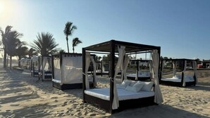 Una playa con varias camas con dosel dispuestas en fila, cada una con dosel y almohadas.