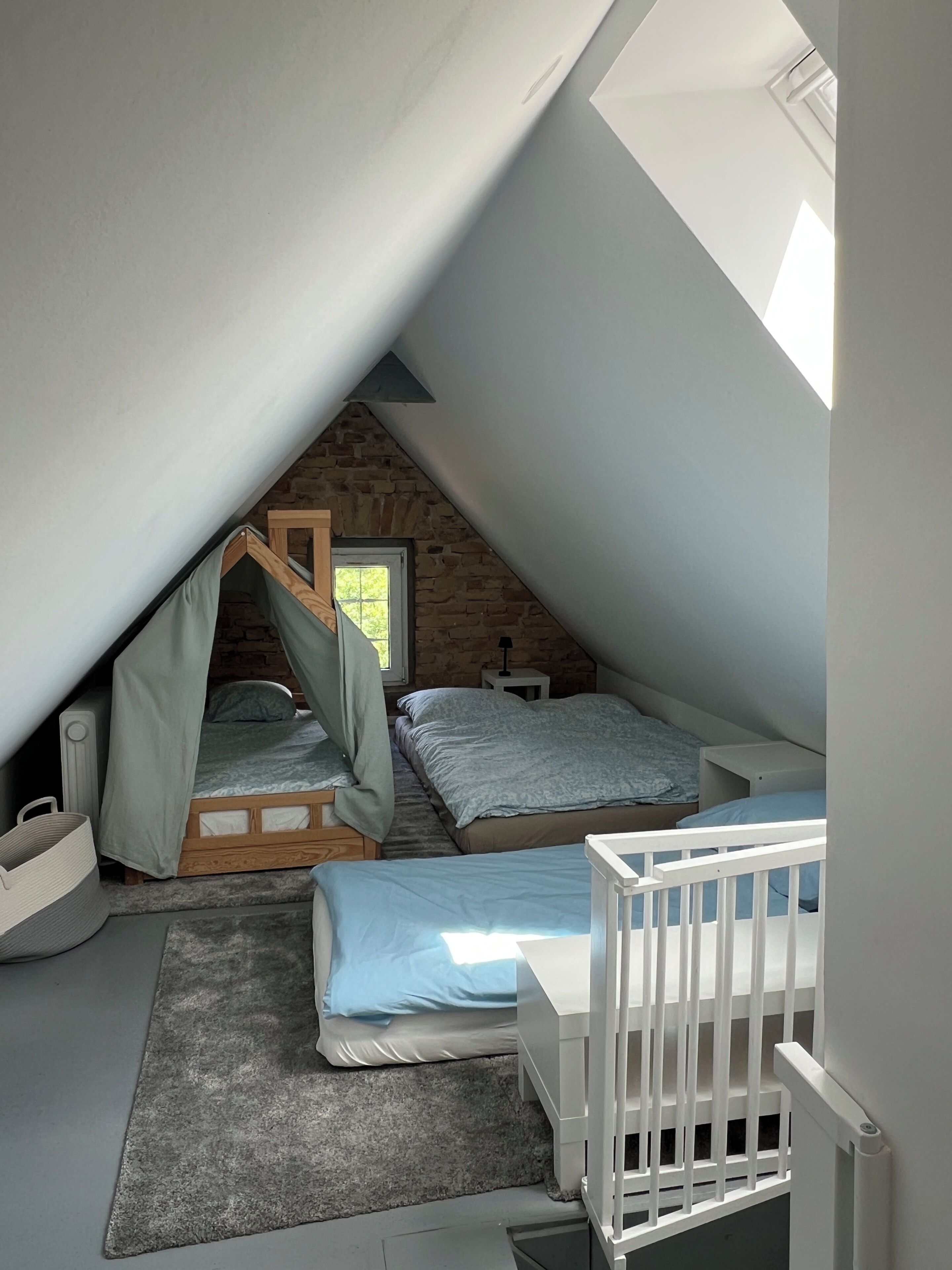 Ein kleines Schlafzimmer unter dem Dach mit Schrägen, zwei Betten, einem Fenster und einer Steinwand.
