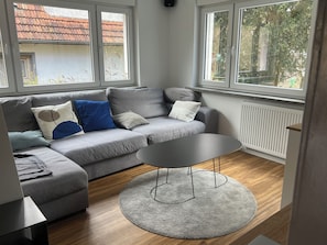 Un salon moderne avec un canapé gris, une table basse ronde et de grandes fenêtres.
