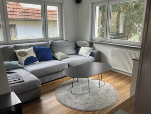A modern living room with a grey sofa, a round coffee table, and large windows.