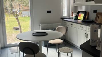 Une cuisine avec des meubles blancs, une table à manger avec des chaises, une fenêtre donnant sur l’extérieur et un plan de travail sur lequel sont disposés divers objets.