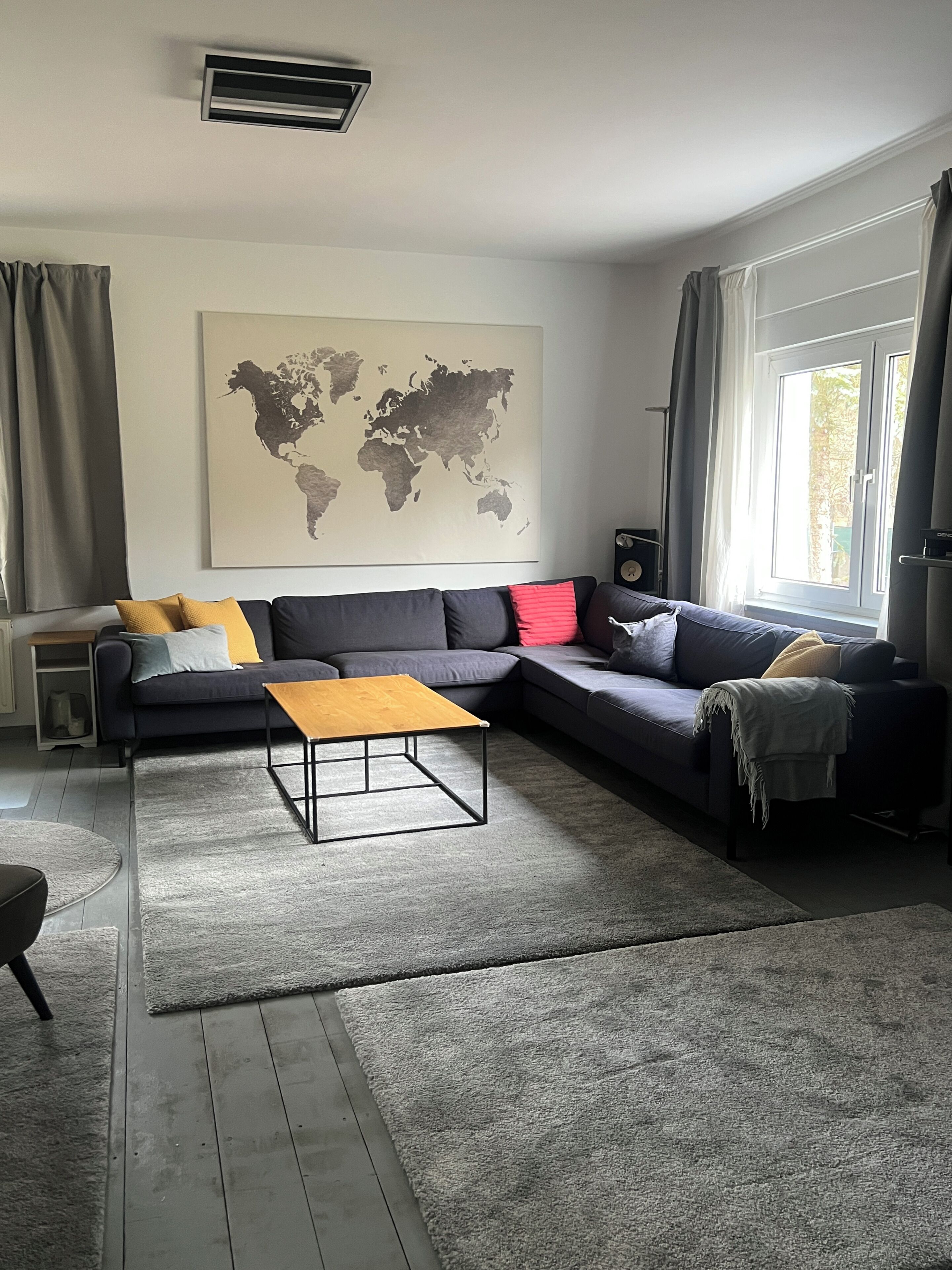 A modern living room with a sectional sofa, a coffee table, a world map on the wall, and a window with curtains.