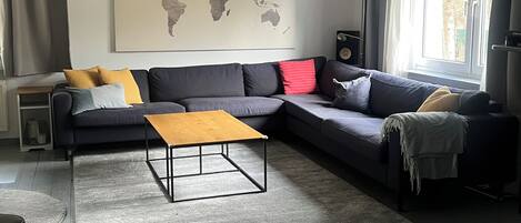 A modern living room with a sectional sofa, a coffee table, a world map on the wall, and a window with curtains.