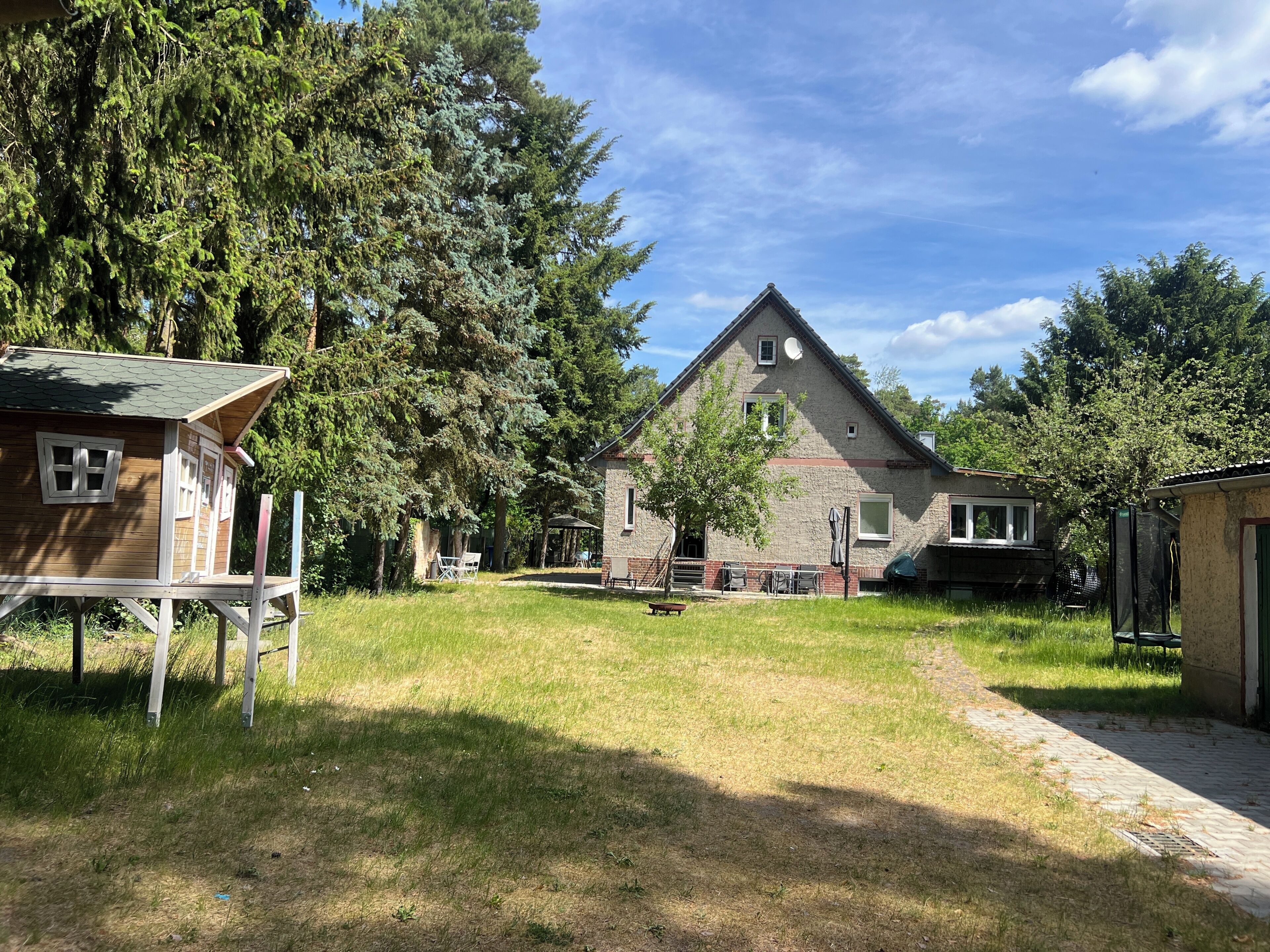 A residential area with a large house, a smaller wooden structure, and a paved pathway.