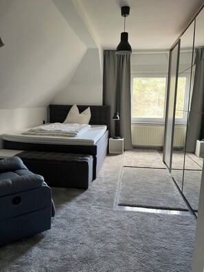 Un dormitorio con cama, mesita de noche, lámpara y vistas al exterior.