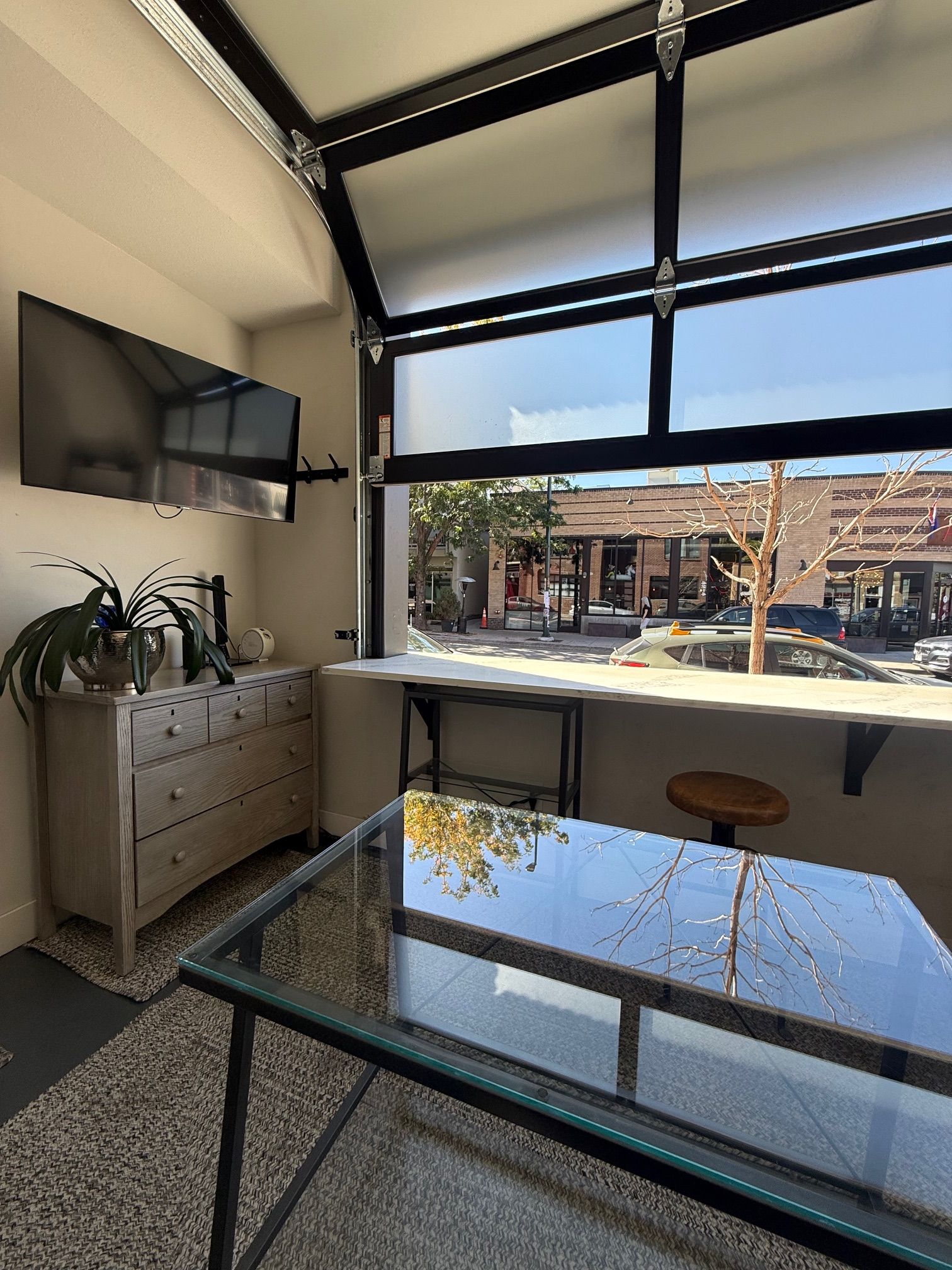 A modern interior with a glass table, a flat-screen TV, and a view of the street outside.