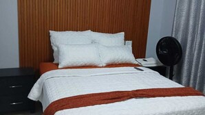 A bed with white bedding and a brown throw, a black bedside table, and a wall with vertical wooden slats. - Pilgrims Corner Guest House  (Westonaria)