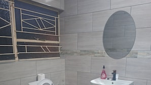 A bathroom with a toilet, sink, and mirror. - Pilgrims Corner Guest House  (Westonaria)