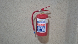 A red fire extinguisher mounted on a textured wall. - Pilgrims Corner Guest House  (Westonaria)