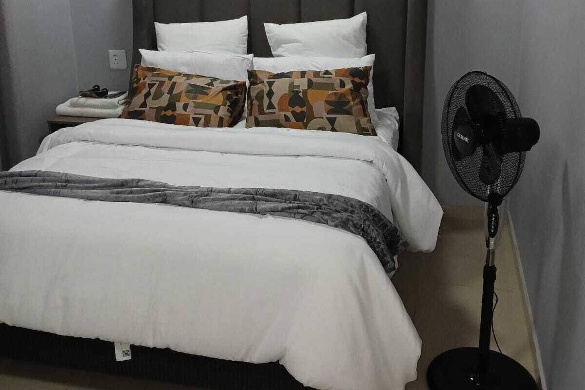 A bedroom with a bed, pillows, a bedside table, a fan, and a ceiling light.