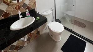 Um banheiro com painel de azulejos, um espelho redondo, uma pia branca, vaso sanitário e chuveiro com box de vidro.