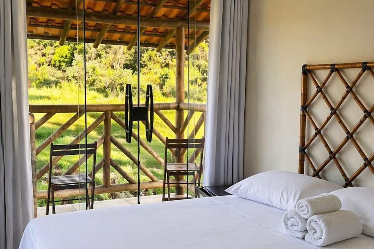 Hotelkamer met een groot bed, een houten hoofdbord, uitzicht op een tuin door een schuifdeur en een airconditioner.