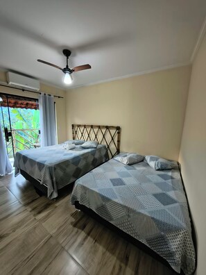 Un dormitorio con dos camas, ventilador de techo y ventana con cortinas.