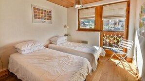 A room with two beds, a window with blinds, a chair, and a hanging light fixture. - Wifi, 2nd floor, terrace, tv, ski locker, 83m², Les Gets (Les Gets)