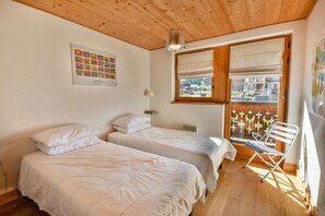 Ein Zimmer mit zwei Betten, einem Fenster mit Jalousien, einem Sessel und einer Pendelleuchte.