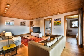 Ein modernes Wohnzimmer mit Holzboden, einer Couch, einem Fernseher und Bildern an den Wänden.