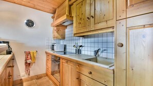 A kitchen with wooden cabinets, a microwave, a sink, and a clock on the wall. - Wifi, 2nd floor, terrace, tv, ski locker, 83m², Les Gets (Les Gets)