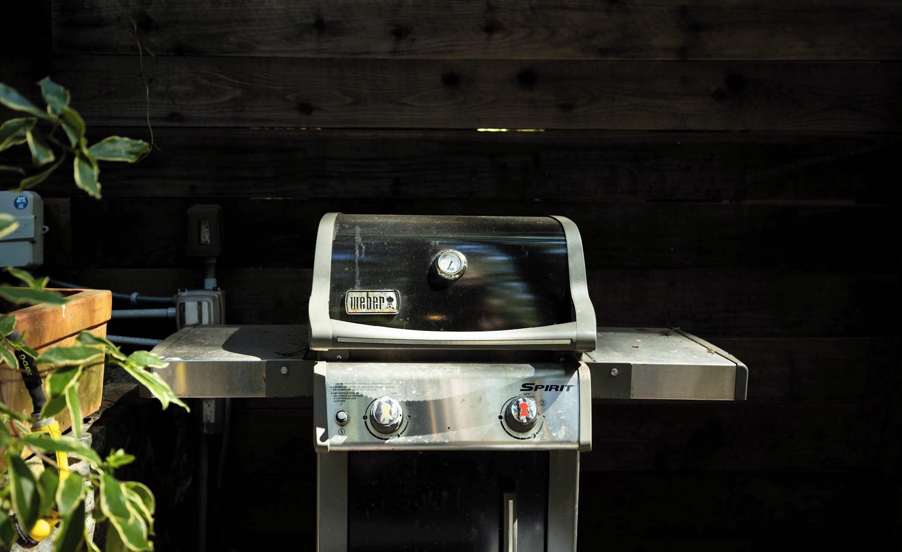 A gas grill with a digital display and control knobs, set against a wooden backdrop.