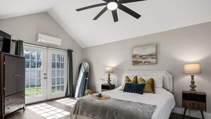 A bedroom with a bed, bedside lamps, a ceiling fan, a window with curtains, and a wall-mounted air conditioner. - Stylish + Trendy Home W/ Office Near It All! (Indianapolis)