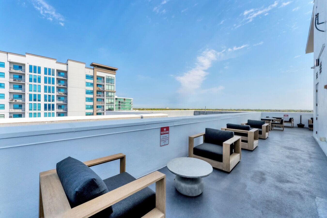 A rooftop terrace with outdoor seating, a view of a building, and a clear sky.