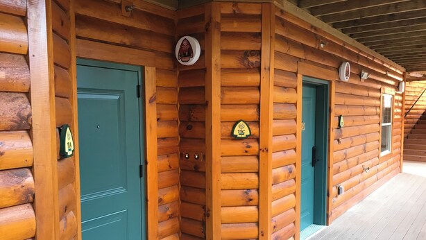 Una cabaña de troncos con fachada de madera, puertas color turquesa y un porche cubierto.